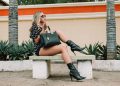 Fashionable woman in boots and sunglasses poses on a bench outdoors.