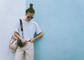 Stylish woman posing with camera in casual attire against a blue wall.